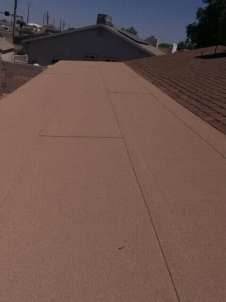 Finished flat roof with tan granulated cap sheet, next to a shingle roof