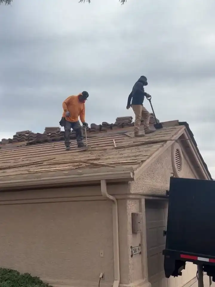 Two crew members on a tile roof, lifting tile and stacking it along the ridge
