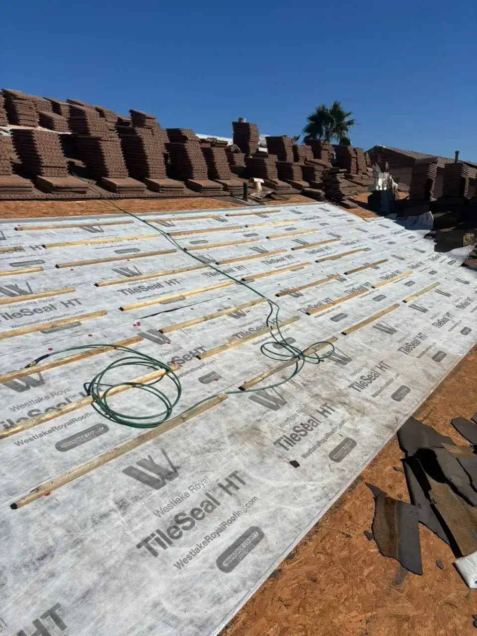 White underlayment rolled out across the roof deck with wood battens on top and tile stacked along the ridge